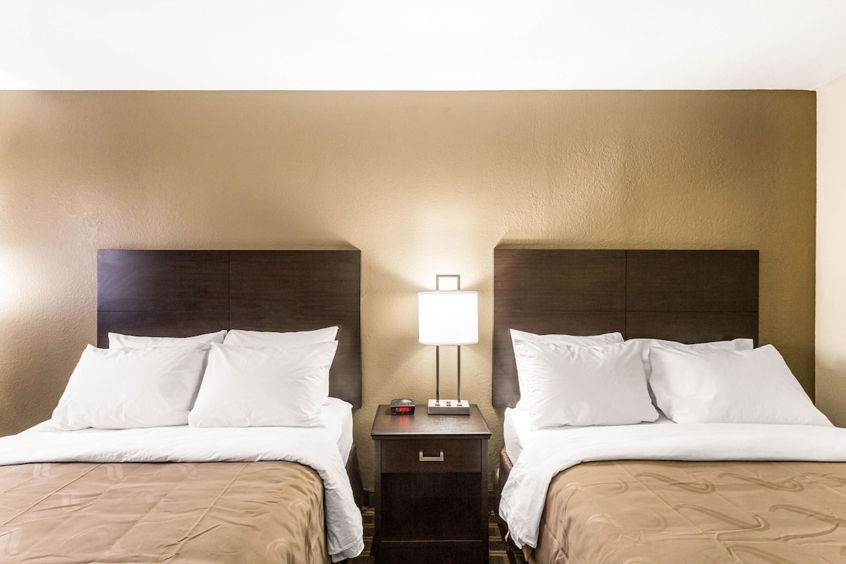 Une chambre d’hôtel avec deux lits, une table de chevet avec une lampe et un petit tiroir.