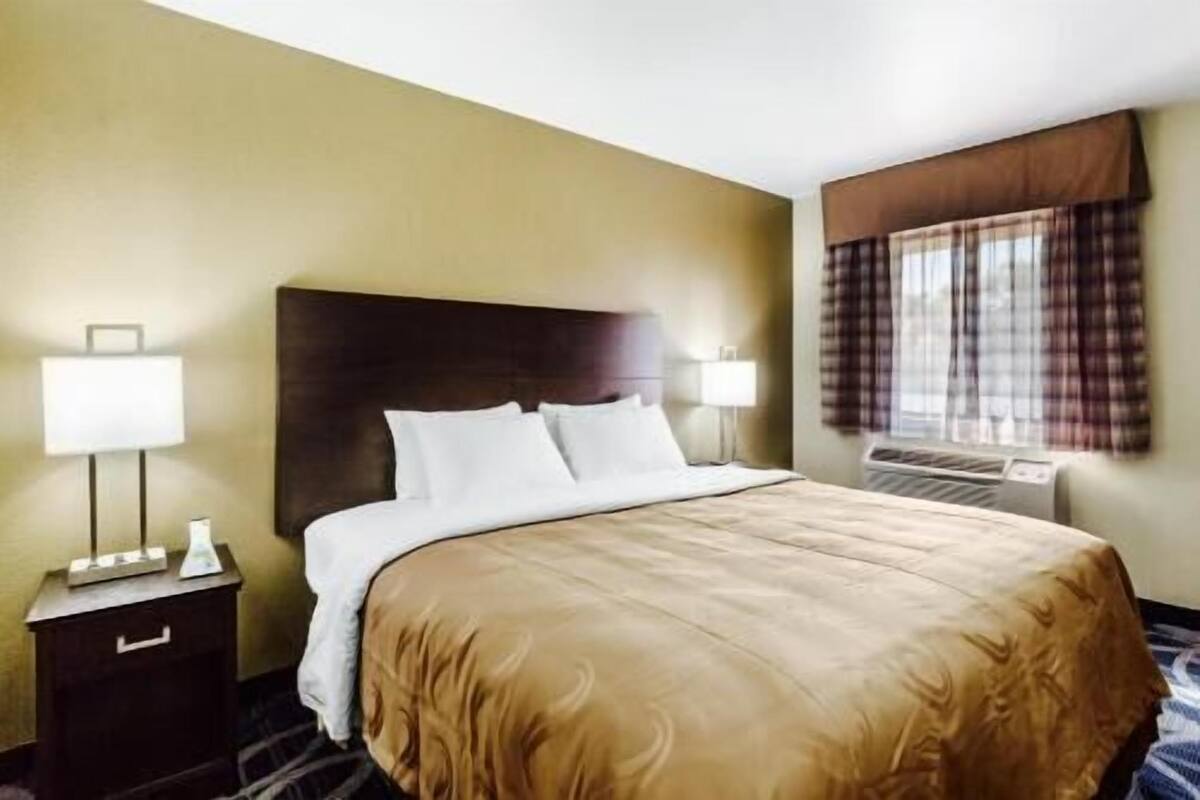 Une chambre d’hôtel avec un grand lit, deux tables de chevet, une fenêtre avec des rideaux et un appareil de climatisation.