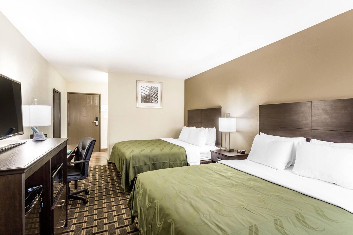 Une chambre d’hôtel avec deux lits, un bureau avec un ordinateur, une chaise et un téléviseur.
