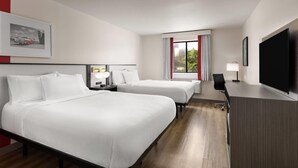 Et hotelværelse med to senge, et skrivebord, et fjernsyn og et vindue med gardiner.