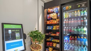 En selvbetjenings kiosk med QR-kode til betaling, en automt til snacks og en drikkemaskine.