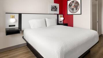 Siististi järjestetty hotellihuone, jossa on suuri sänky, yöpöydät lampuineen ja seinillä olevat taulut.