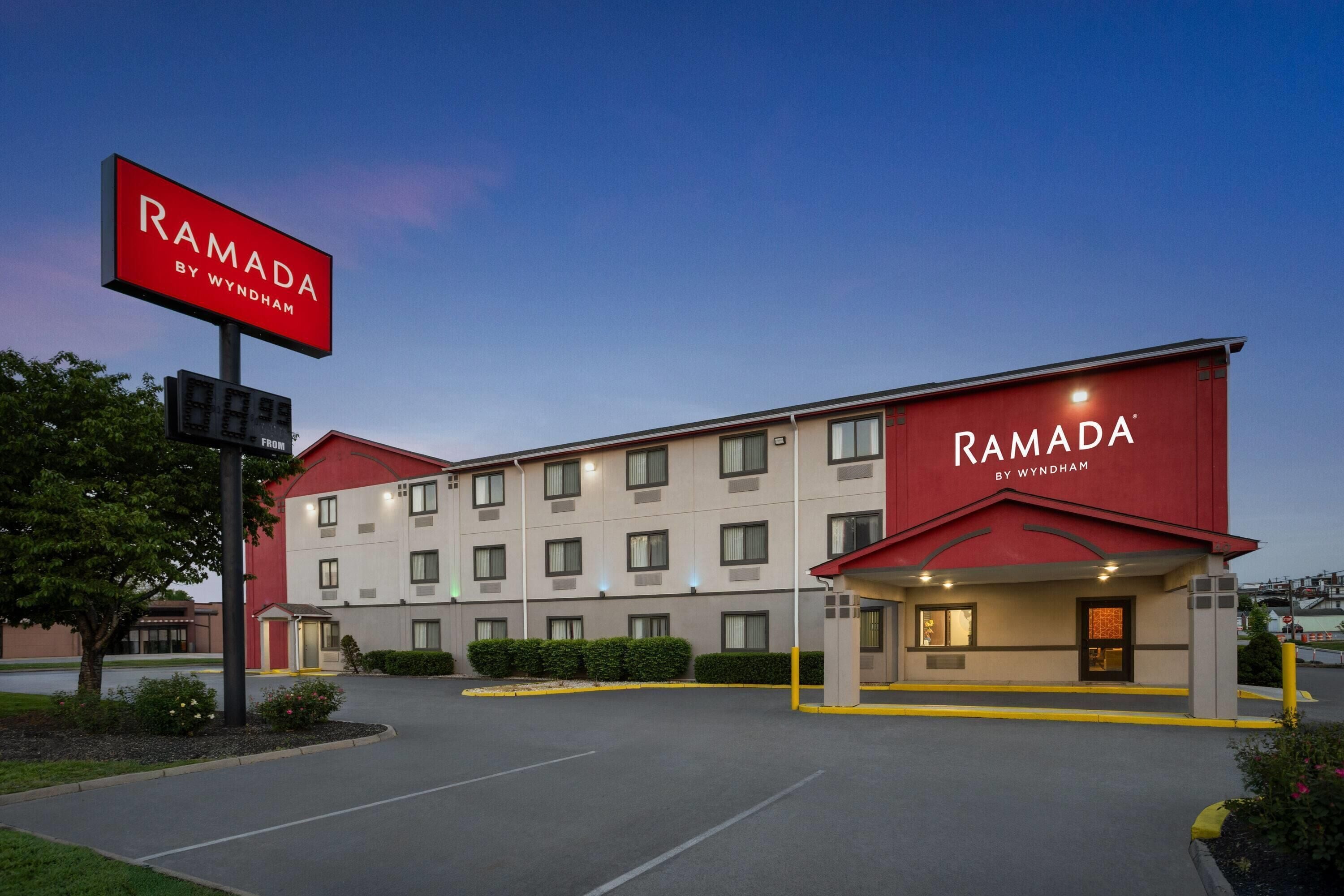 Ein Ramada by Wyndham Hotel mit roter und weißer Fassade, einem Parkplatz und blauem Himmel.
