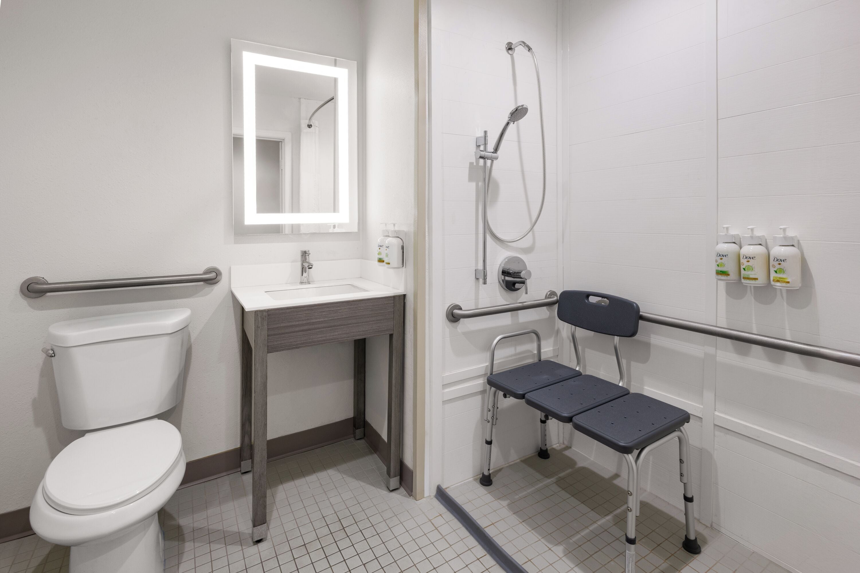 A modern bathroom with a toilet, sink, mirror, shower, and a wheelchair-accessible bench.