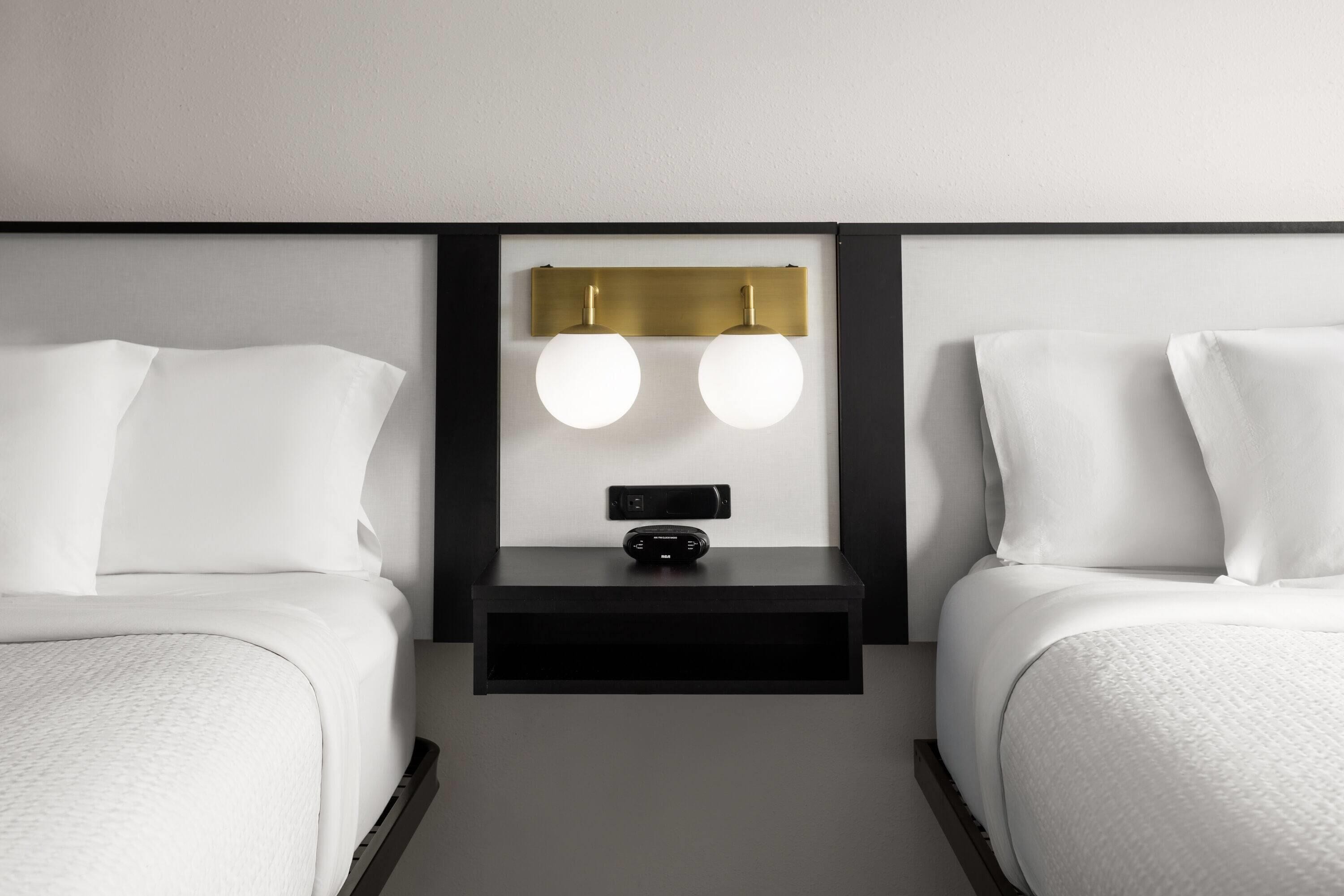 Una habitación de hotel con dos camas, una mesita de noche con lámpara y una lámpara de pared.