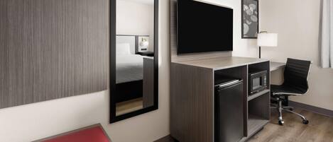Una habitación de hotel moderna con una televisión de pantalla plana grande, un escritorio con una silla, un microondas y un banco rojo.