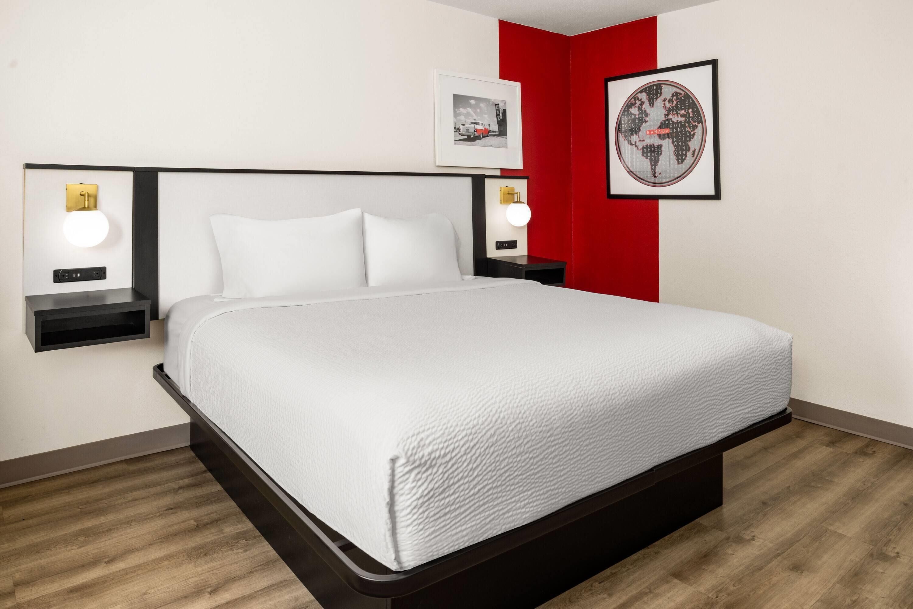 A neatly made bed in a hotel room with a white headboard, two bedside tables with lamps, and a red accent wall.