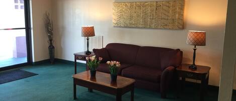 A lobby with a red sofa, two lamps, a coffee table with flowers, and a wall art piece.