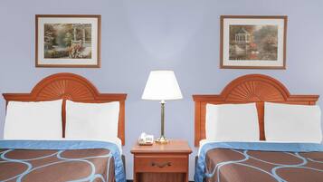 Quarto de hotel com duas camas, uma mesa de cabeceira com abajur e duas molduras na parede.