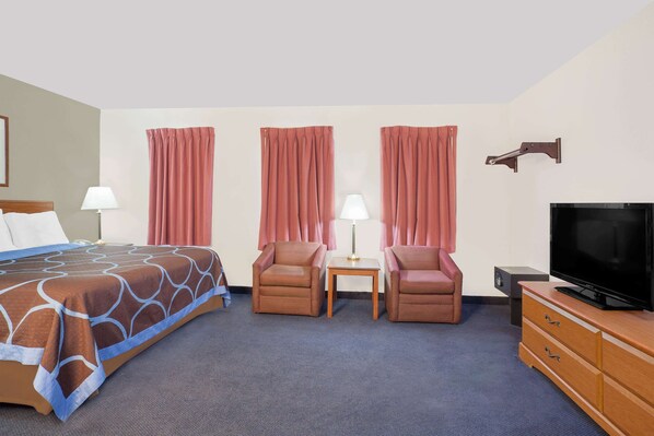 A hotel room with a bed, two armchairs, a small table, a TV, and a dresser. - Super 8 by Wyndham Middletown (Middletown)