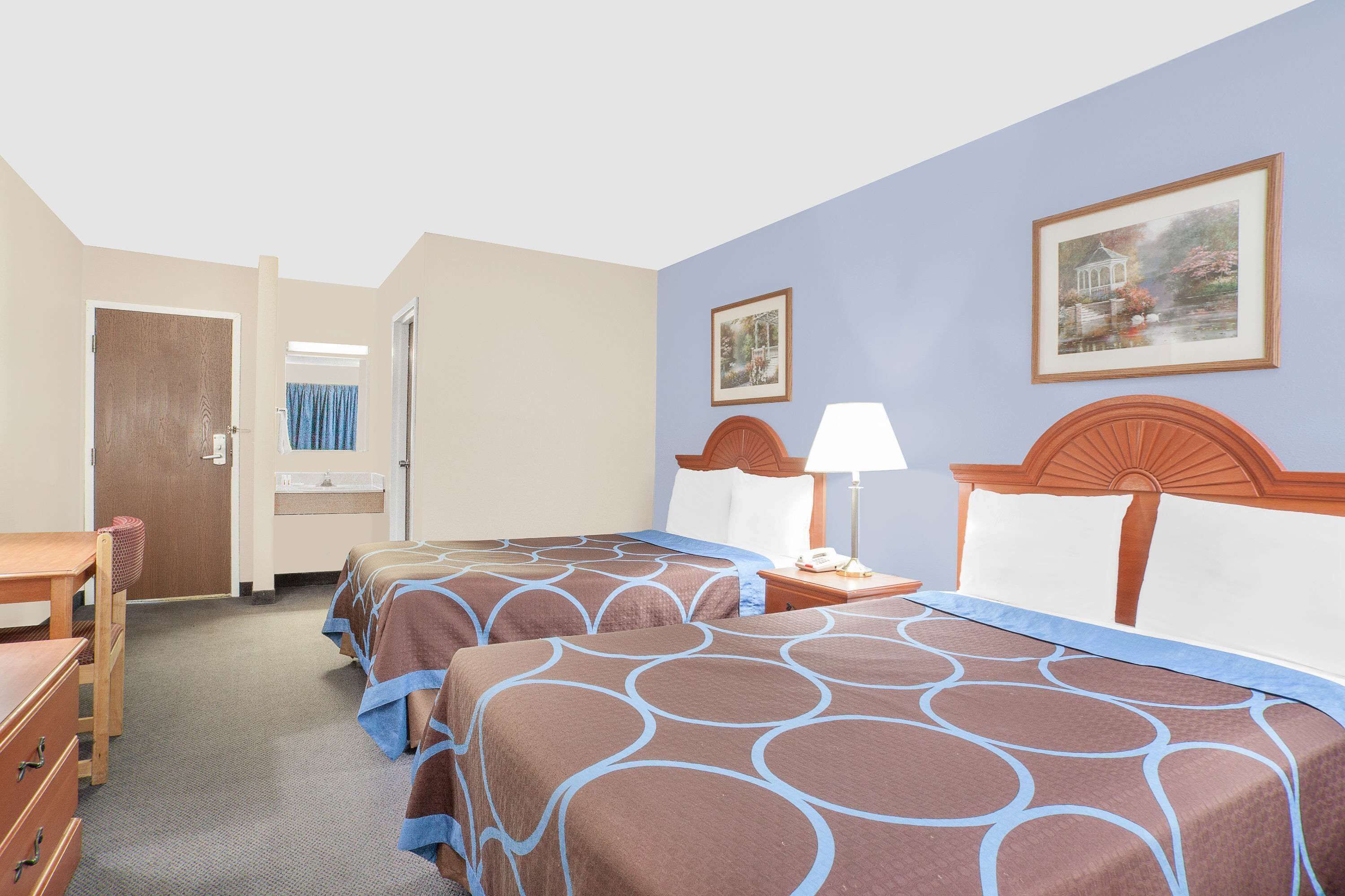 A hotel room with two beds, a desk, a chair, a nightstand, and a lamp.