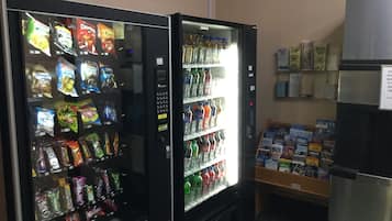 A vending machine with snacks and drinks, a small display of magazines, and a refrigerator.