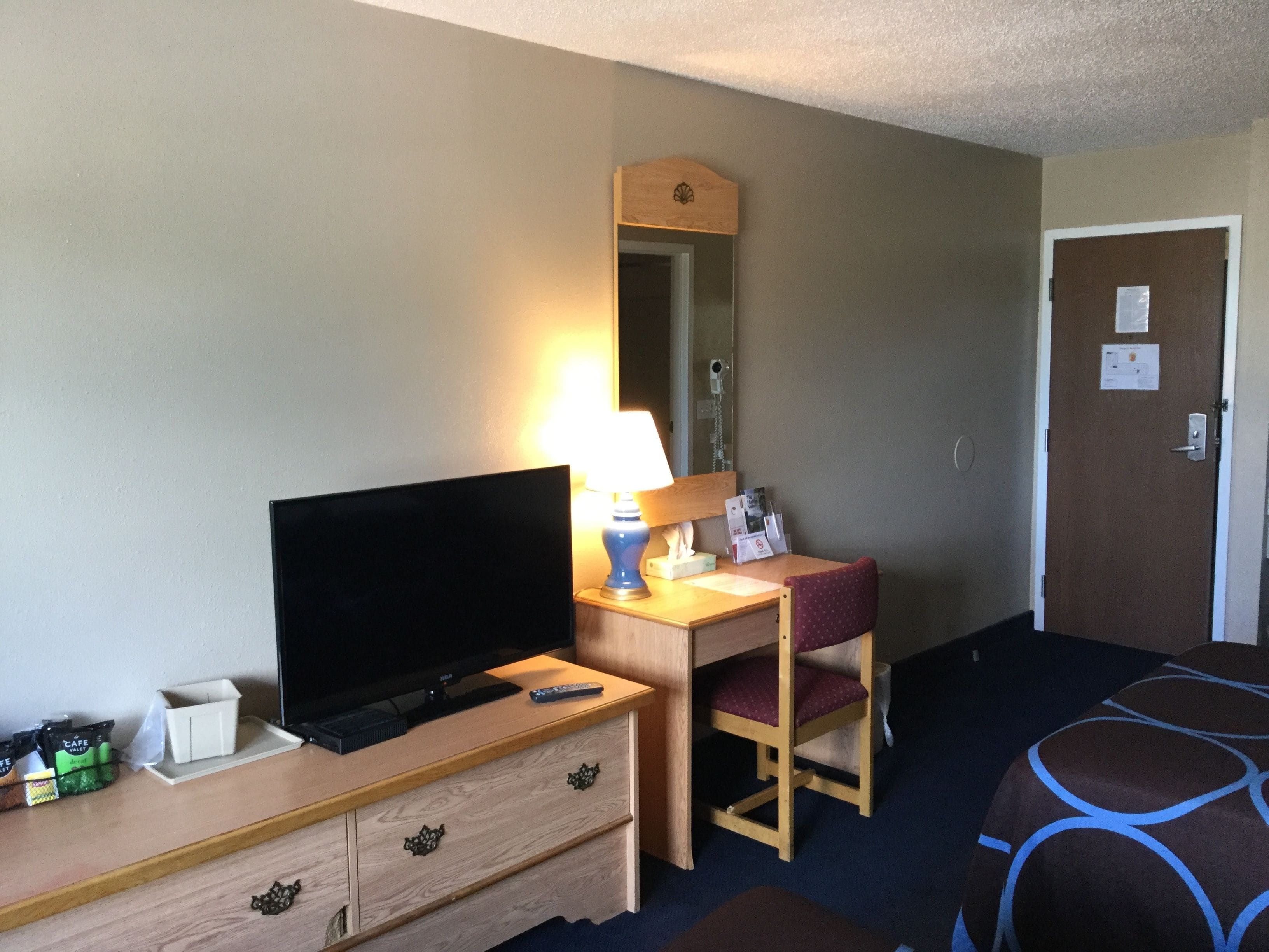 Una habitación de hotel con televisión, escritorio con lámpara, silla y cama.