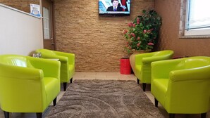 A reception area with a stone wall, a television mounted on the wall, and two bright green chairs facing each other. - Super 8 by Wyndham Plattsburgh (Plattsburgh)