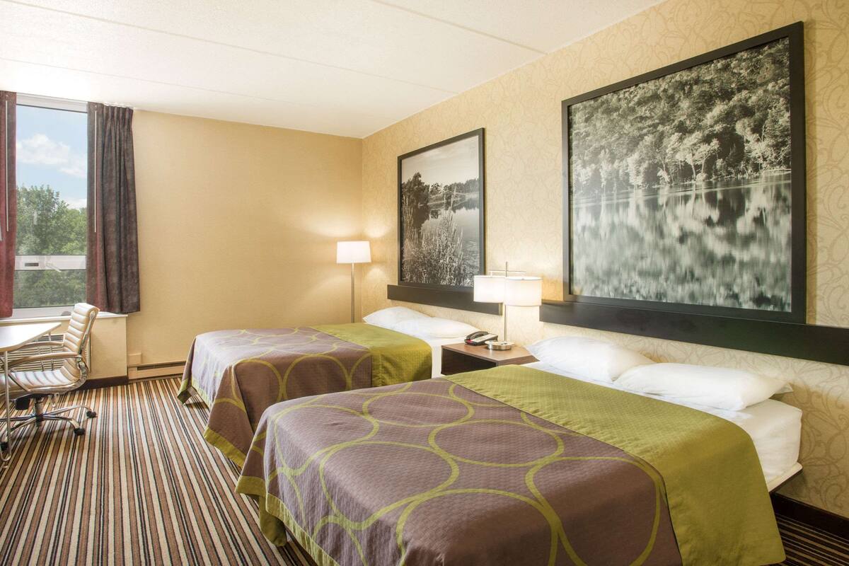 A hotel room with two beds, a desk, and a chair. There are two nightstands with lamps.