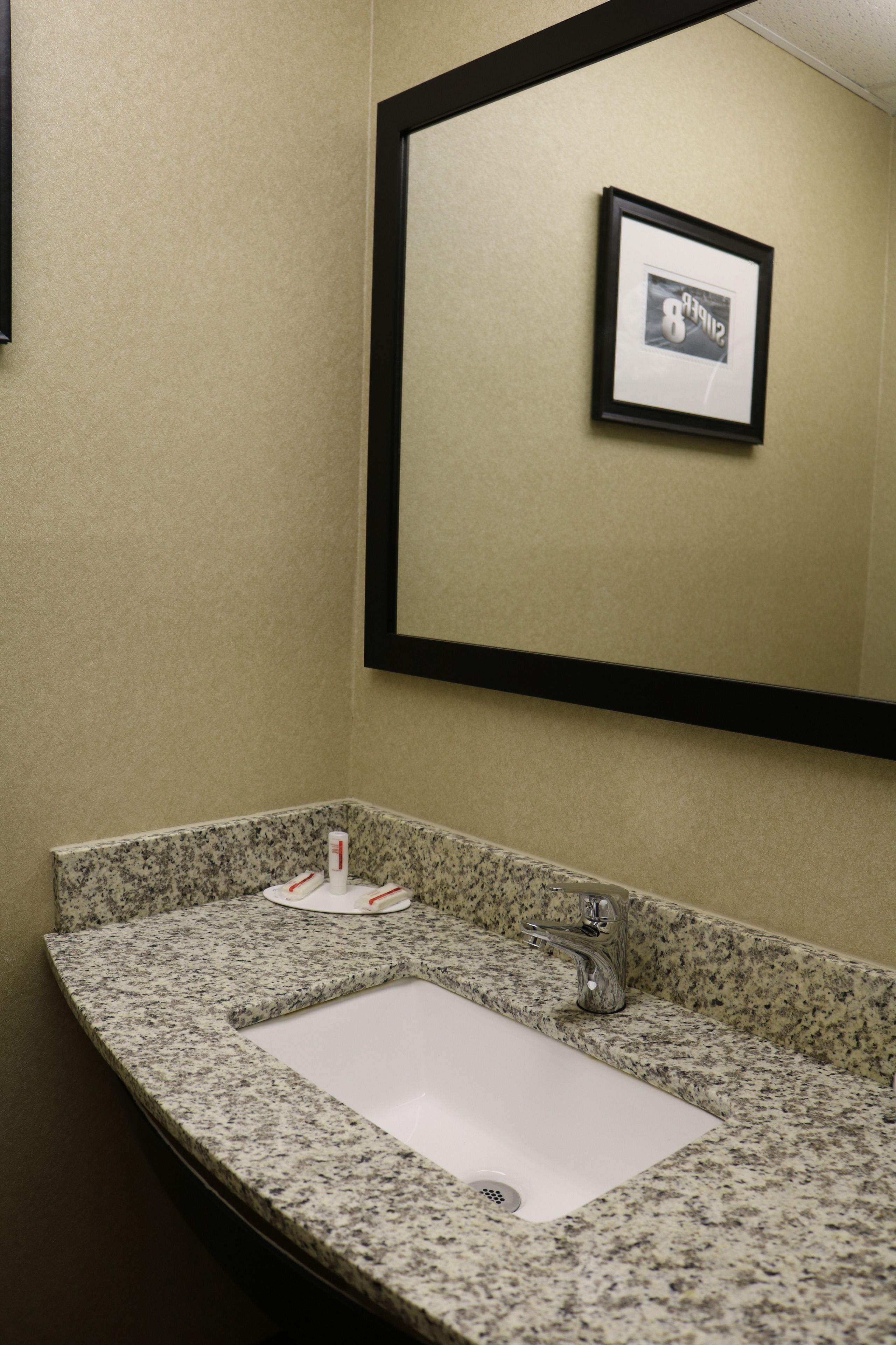 A bathroom with a granite countertop, a white sink, a mirror, and a framed picture on the wall.