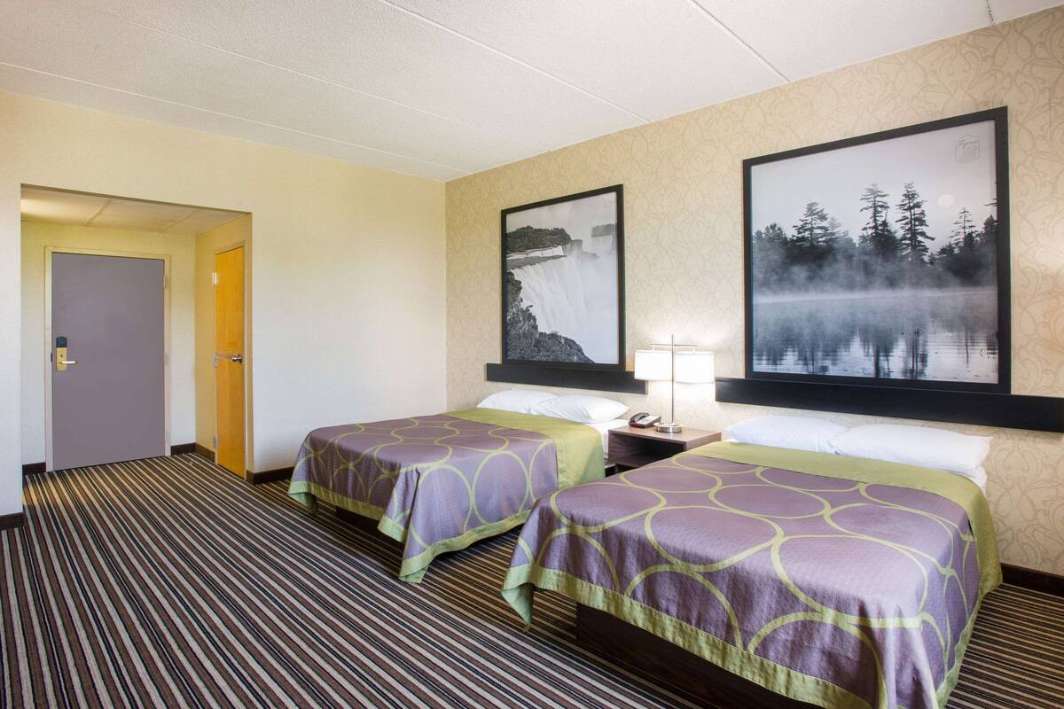 A hotel room with two beds, a carpeted floor, and two framed pictures on the wall.