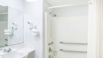 A bathroom with a sink, mirror, towel rack, and shower with grab bars.