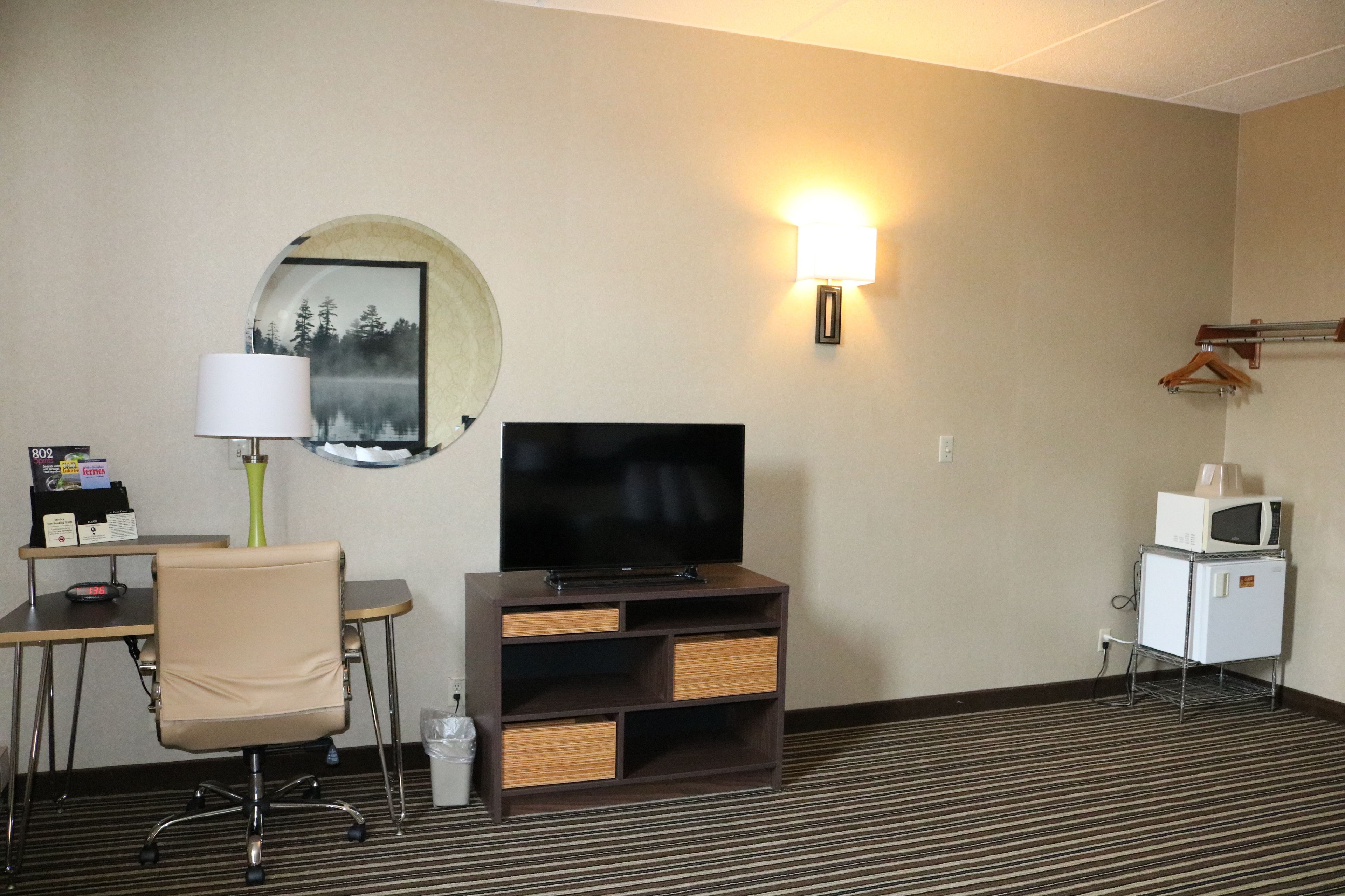 Ein Hotelzimmer mit Flachbildfernseher, Schreibtisch mit Lampe, Stuhl, Kleiderhaken und Mikrowelle.