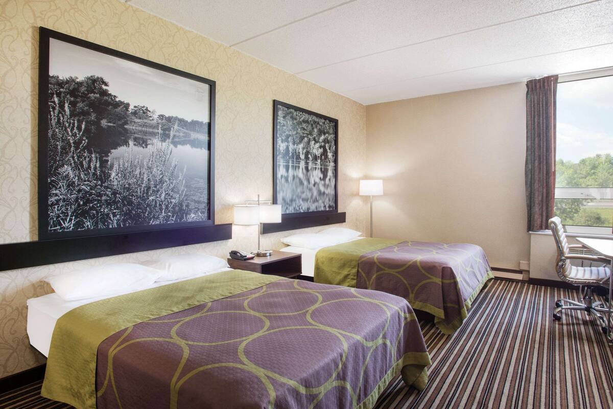A hotel room with two beds, a desk, a chair, and two large framed pictures on the wall.
