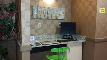 A business center with a computer desk, a green chair, a painting of trees, and a 'Business Center' sign.