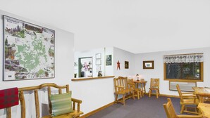 A room with a wooden bench, a table, and chairs. There is a map on the wall and a window with a curtain. - Super 8 by Wyndham Lake George/Warrensburg Area (Lake George)