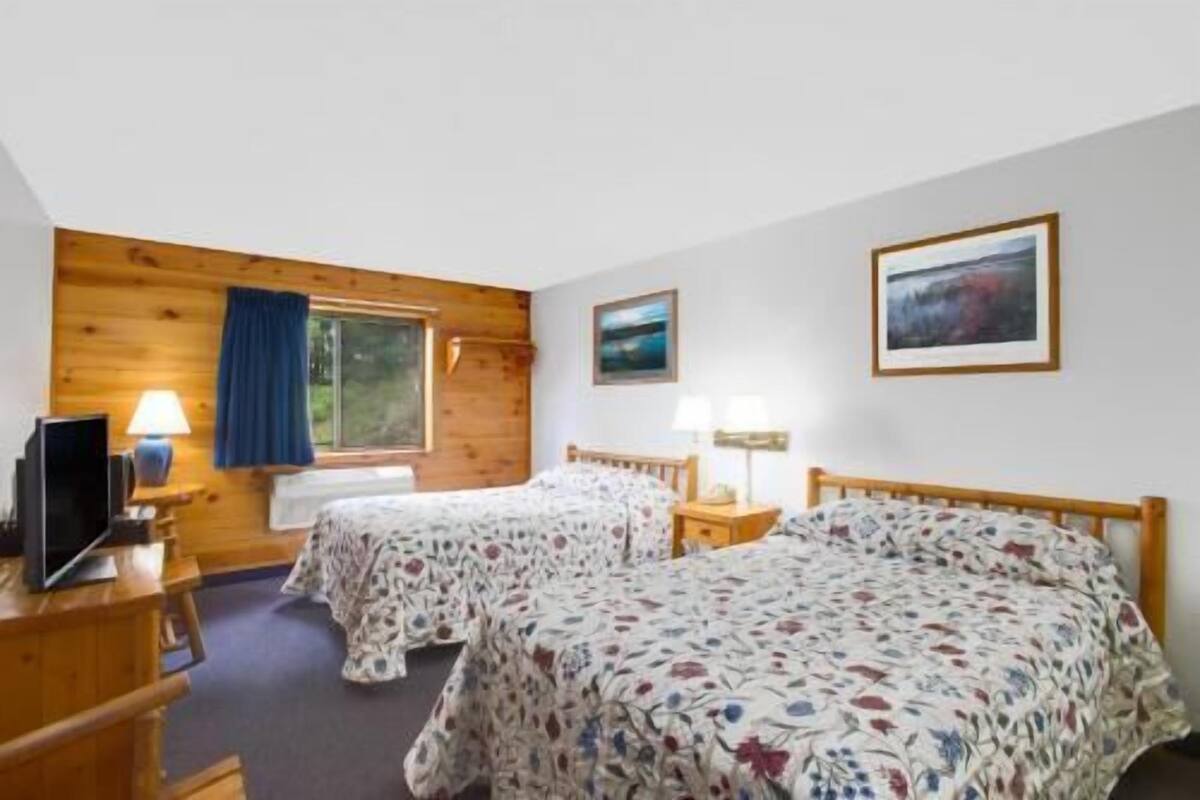 Een kamer met twee bedden, een bureau, een televisie en een raam met gordijnen.