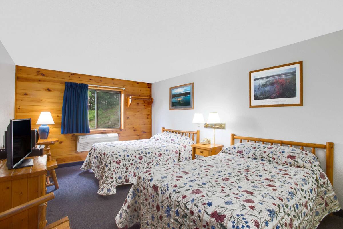 Een kamer met twee bedden, houten wanden, een raam, een bureau met een computer en een lamp.