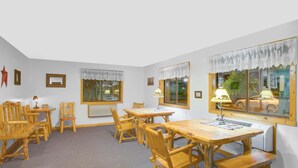 A room with a wooden dining table and chairs, a window with lace curtains, and a radiator. - Super 8 by Wyndham Lake George/Warrensburg Area (Lake George)