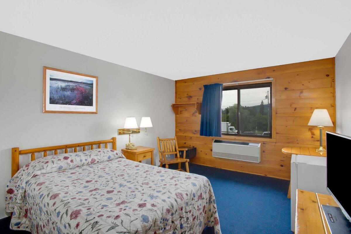 Een kamer met een bed, een bureau, een stoel, een televisie en een raam met gordijnen.