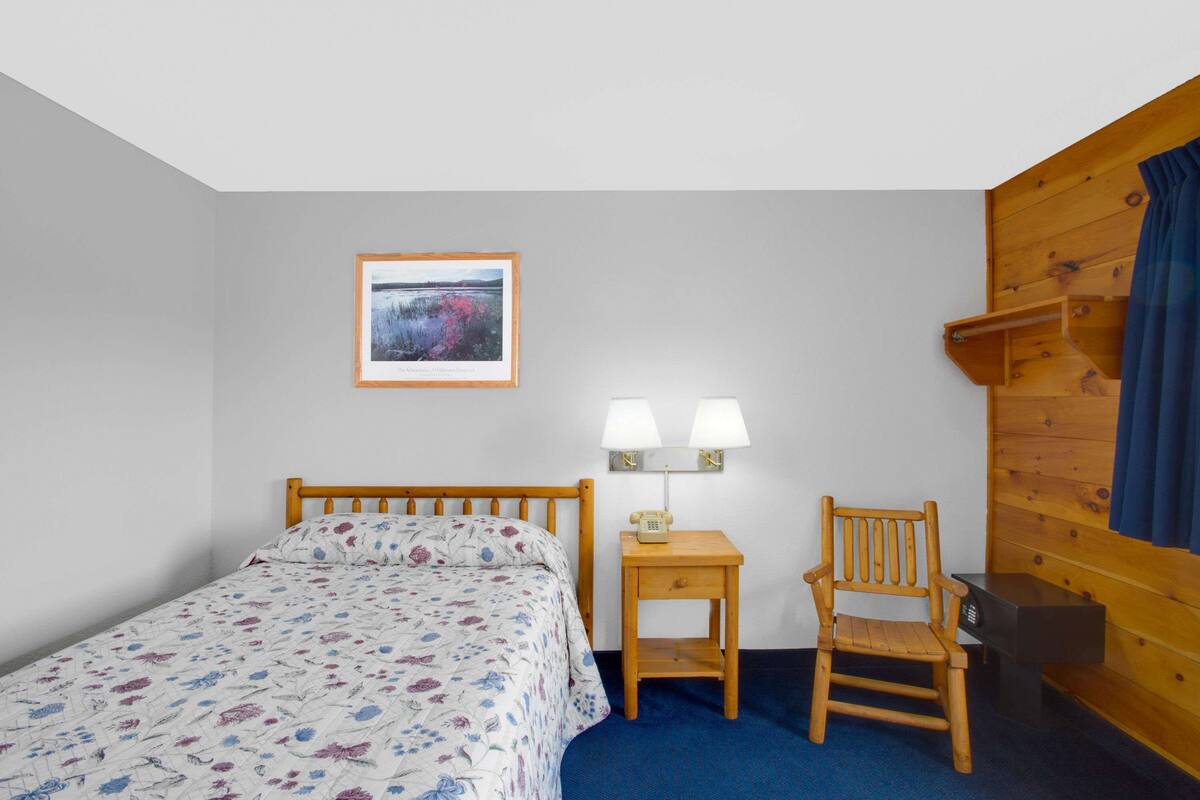 Een slaapkamer met een houten bed, een nachtkastje met een lamp, een stoel en een houten wandpaneel.