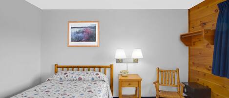 A bedroom with a wooden bed, a nightstand with a lamp, a chair, and a wooden wall panel.