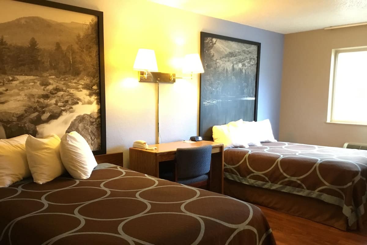 Ein Hotelzimmer mit zwei Betten, einem Schreibtisch, einem Stuhl, einer Lampe und einem Bild an der Wand.