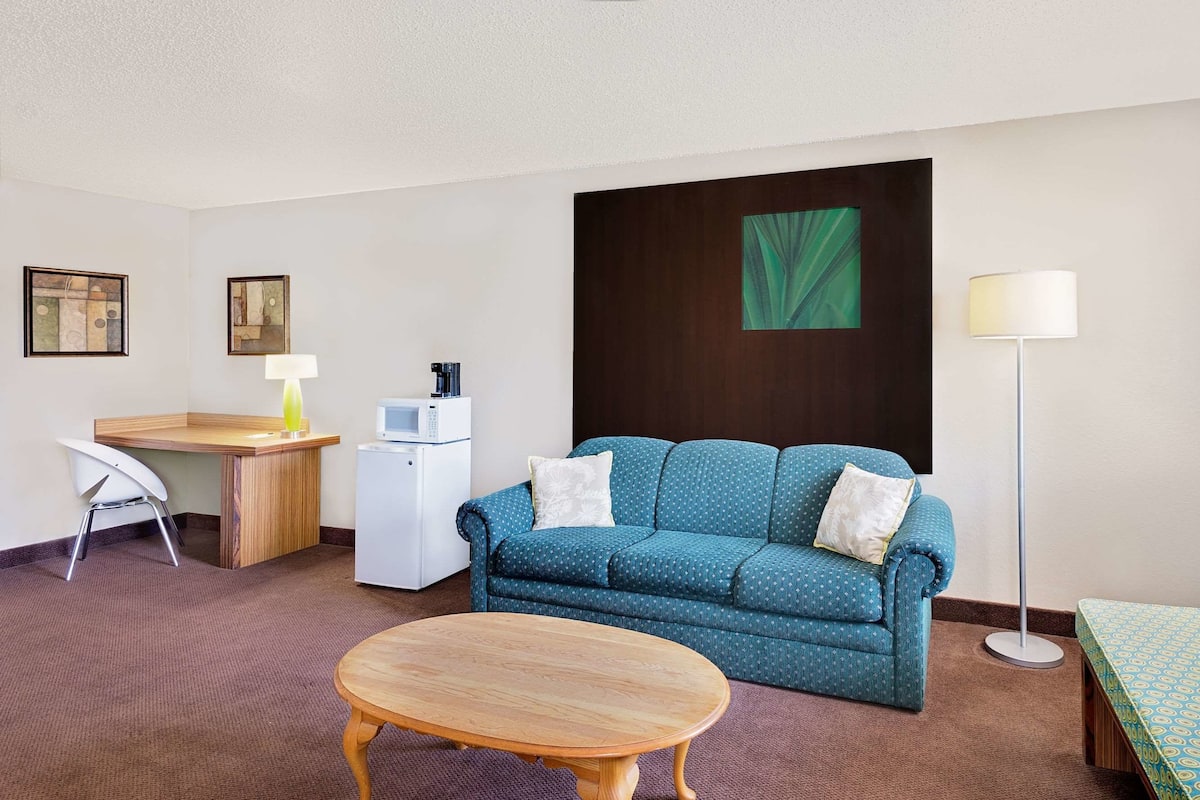 Ein gemütliches Hotelzimmer mit einem blauen Sofa, einem Holztisch, einem weißen Kühlschrank, einer Lampe und einem kleinen Tisch.