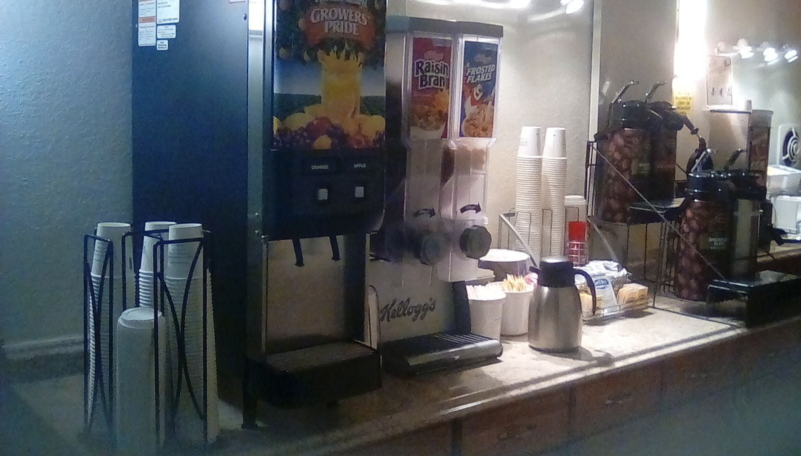 Una máquina de café, un dispensador de bebidas y vasos apilados sobre una encimera.