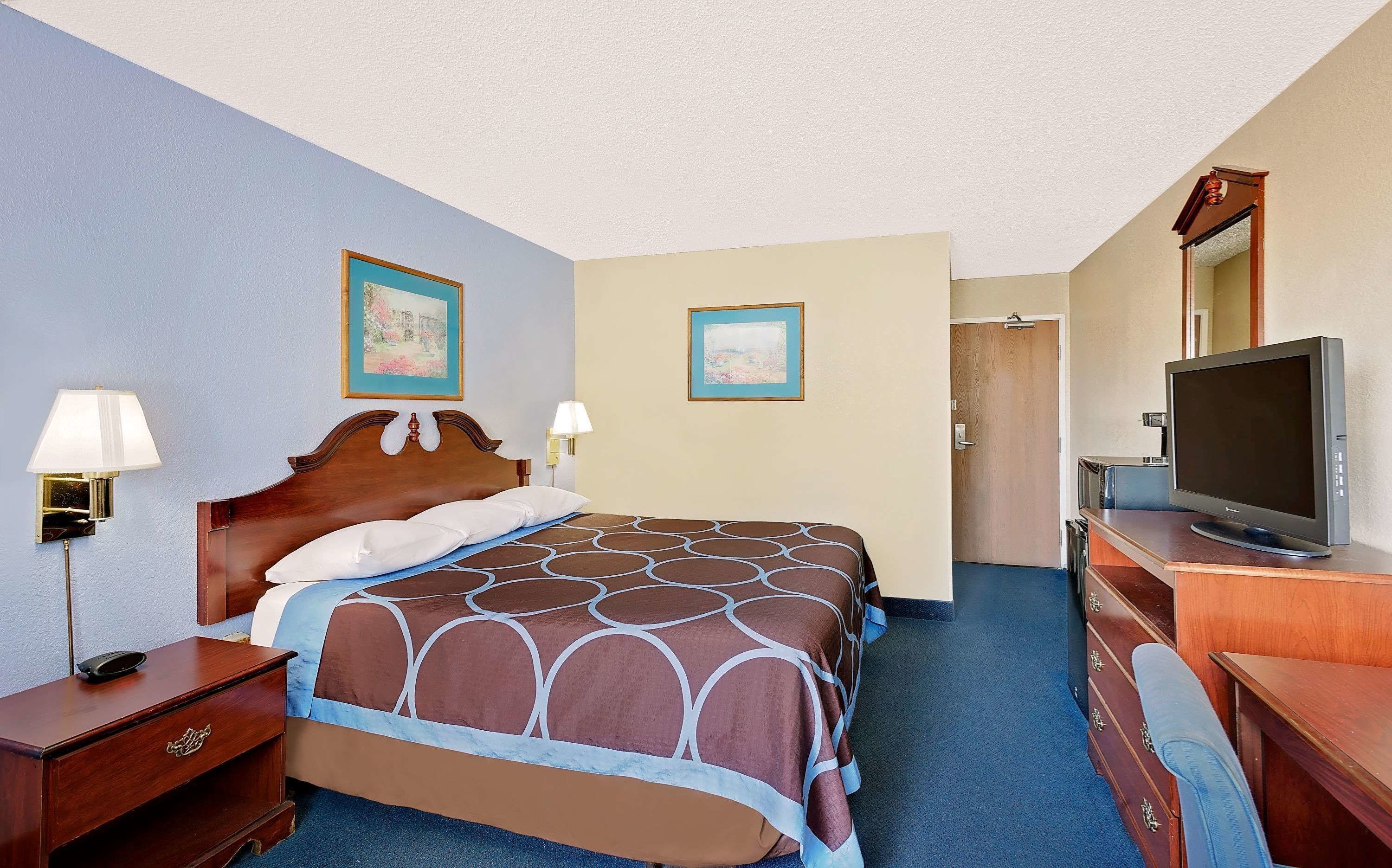 Habitación de hotel con cama, televisión, escritorio y dos lámparas de pared.