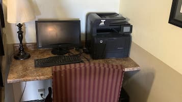 Une chambre d’hôtel compacte équipée d’un bureau, d’un écran d’ordinateur, d’une imprimante et d’une chaise à rayures.