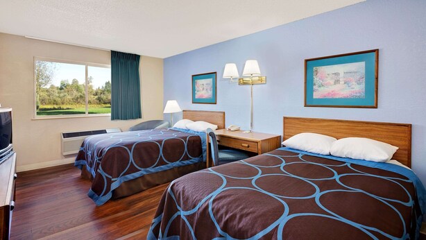 A hotel room with two beds, a desk, a chair, a lamp, and a window with a view of greenery. - Super 8 by Wyndham Newburgh/West Point Near Stewart Airport (Newburgh)