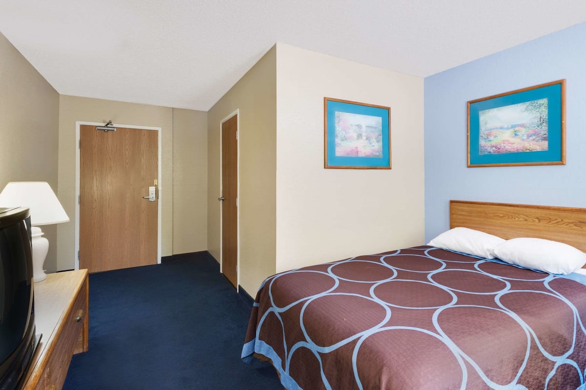Ein Hotelzimmer mit einem Bett, einem Schreibtisch, einem Sessel, einer Lampe und zwei gerahmten Bildern an der Wand.