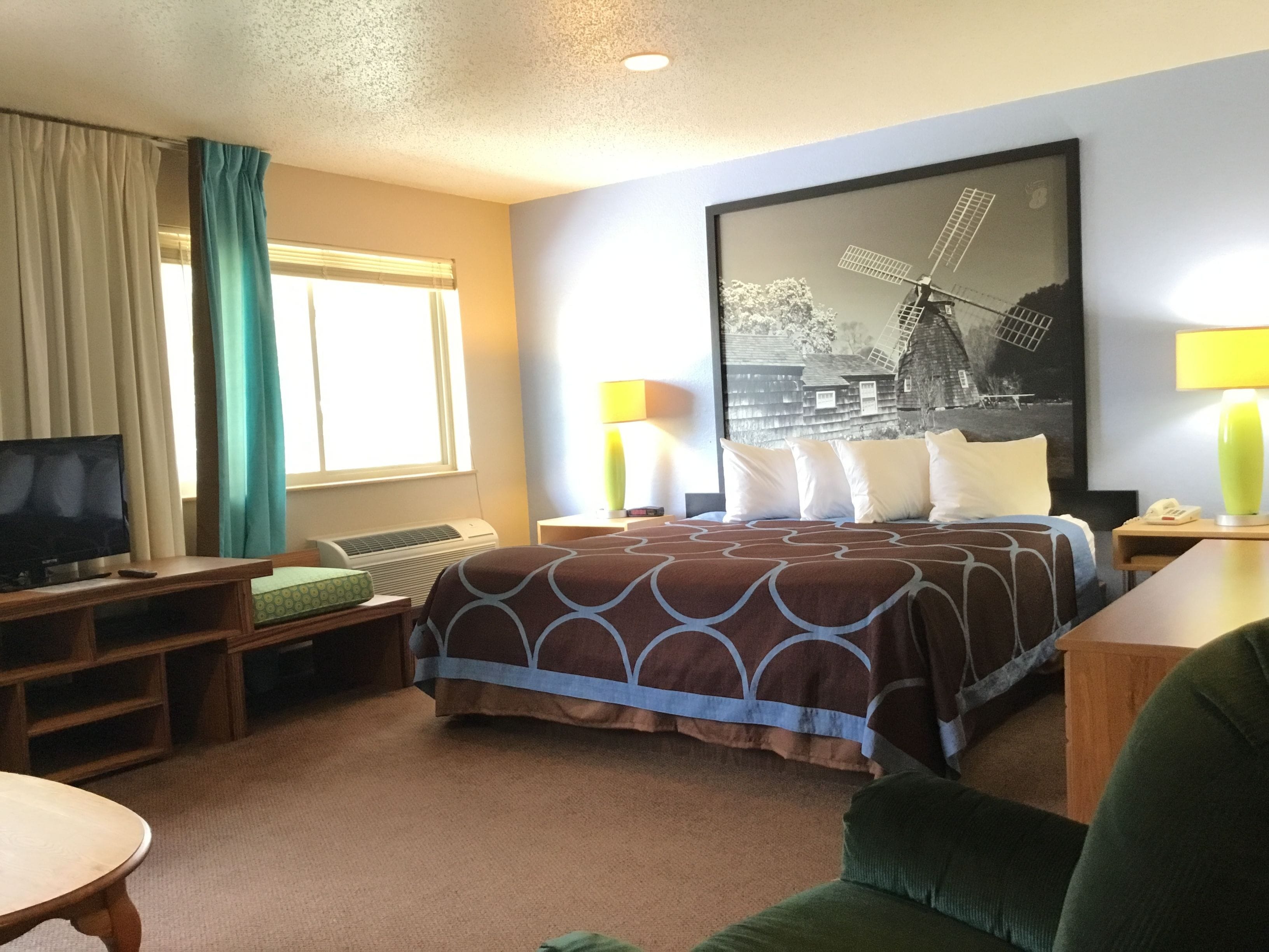 Una habitación de hotel con cama, televisión, escritorio, lámpara y ventana con cortinas.