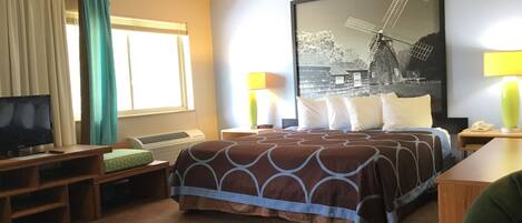 Una habitación de hotel con cama, televisión, escritorio, lámpara y ventana con cortinas.