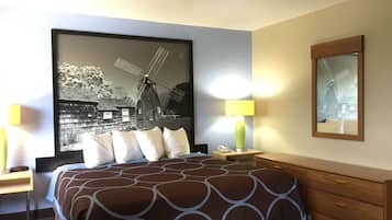 A hotel room with a large bed, a nightstand, a lamp, a dresser, and a framed picture of a windmill.
