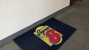 A hotel reception desk with a Super 8 logo on the carpet, a framed picture on the wall, and a warning sign about government regulations. - Super 8 by Wyndham Newburgh/West Point Near Stewart Airport (Newburgh)