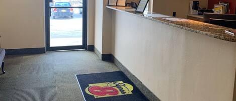 Eine Hotellobby mit einer Rezeption, einem Hinweisschild für den Ausgang und einer Fußmatte mit einem Logo.