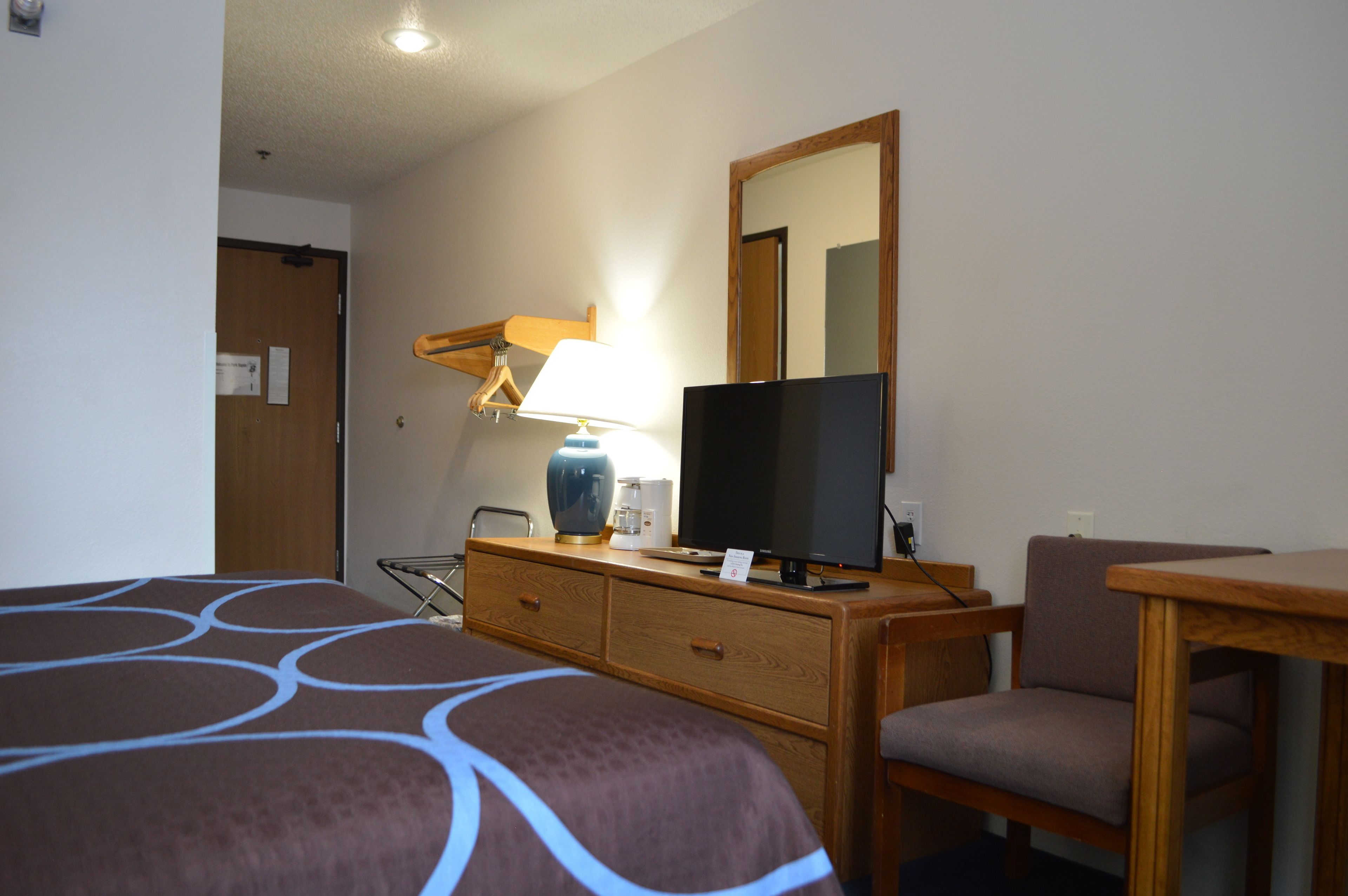 Habitación de hotel con cama, televisión, cómoda de madera, silla y escritorio.