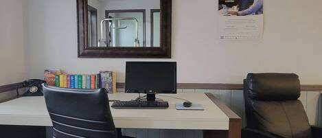 A desk with a computer, a chair, and a mirror. There are books on the desk and a poster on the wall.