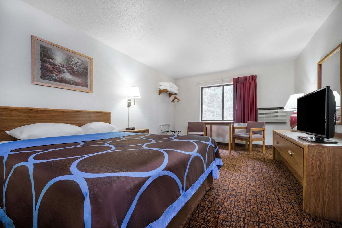 Une chambre d’hôtel avec un grand lit, un bureau, une chaise, une télévision, une fenêtre avec des rideaux et un tableau au mur.