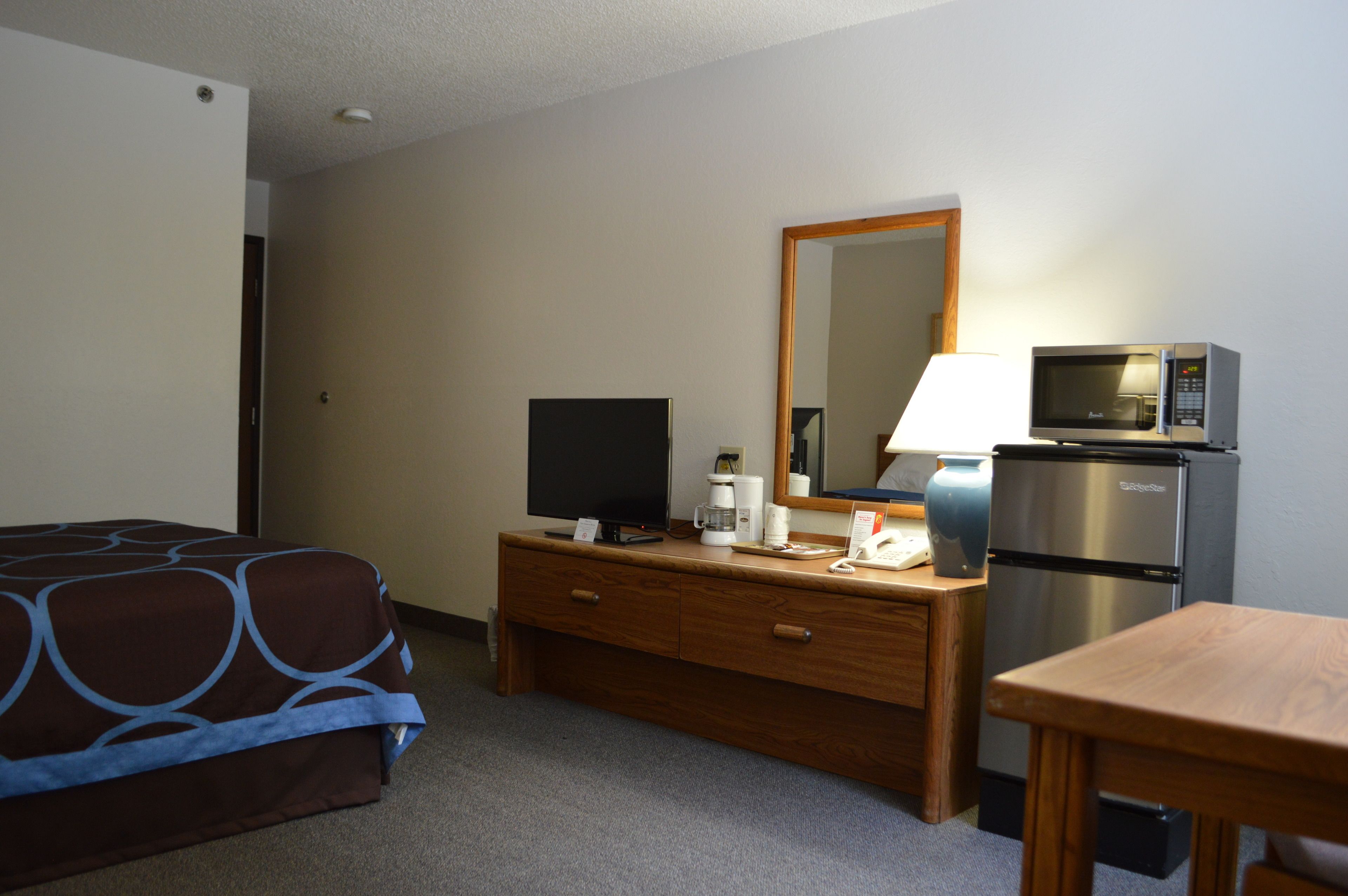Une chambre d’hôtel équipée d’un lit, d’une commode en bois, d’une télévision, d’un four à micro-ondes et d’un réfrigérateur.