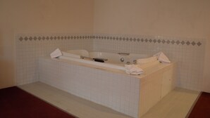 Un baño con una bañera grande, paredes de azulejos y piso rojo.
