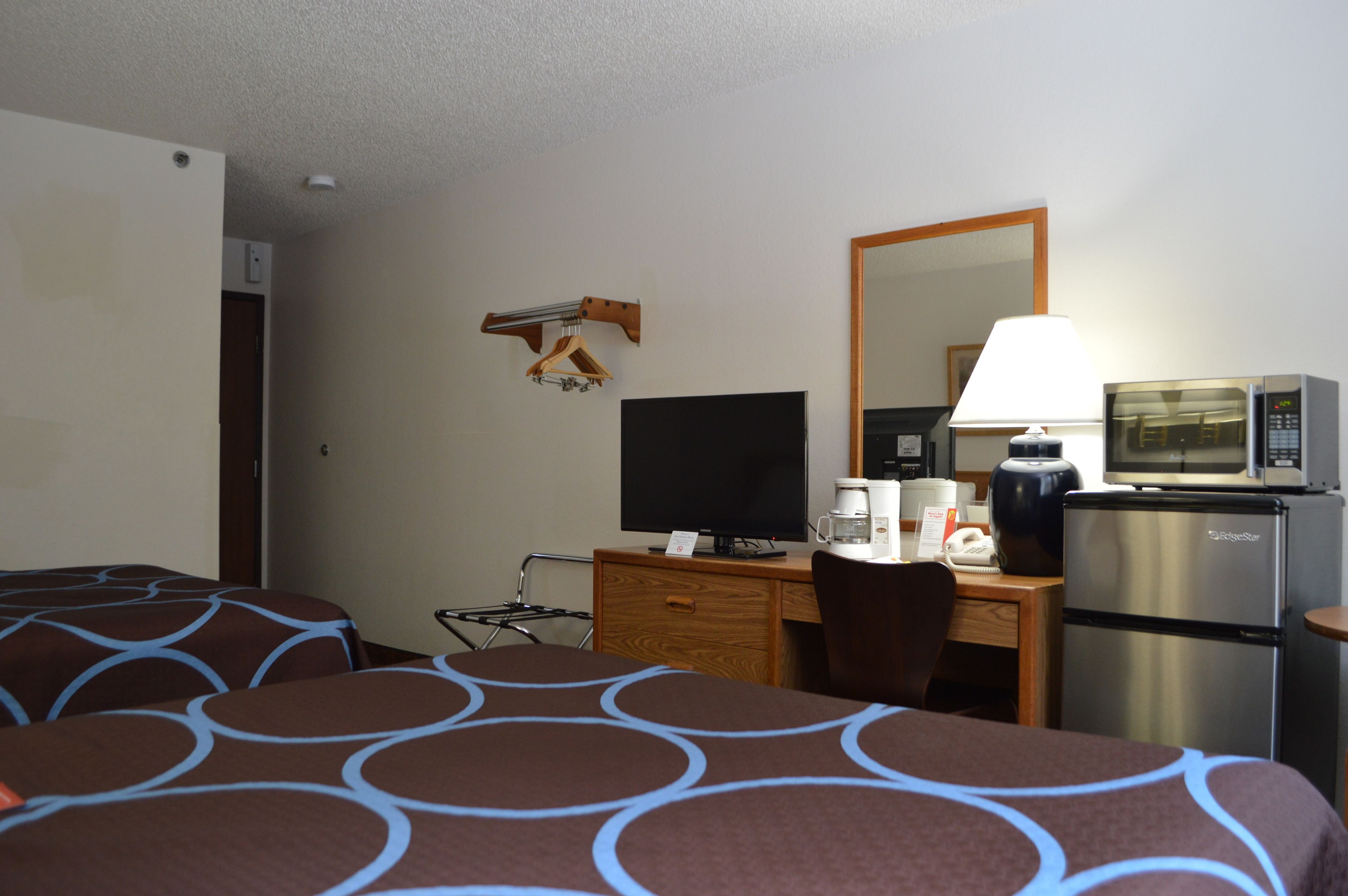A hotel room with two beds, a desk with a computer, a refrigerator, and a microwave.